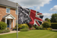 A flag on a silver pole flying outdoors in front of a suburban house. The flag combines a black-and-white lion head on the left with a distressed Union Jack design on the right.